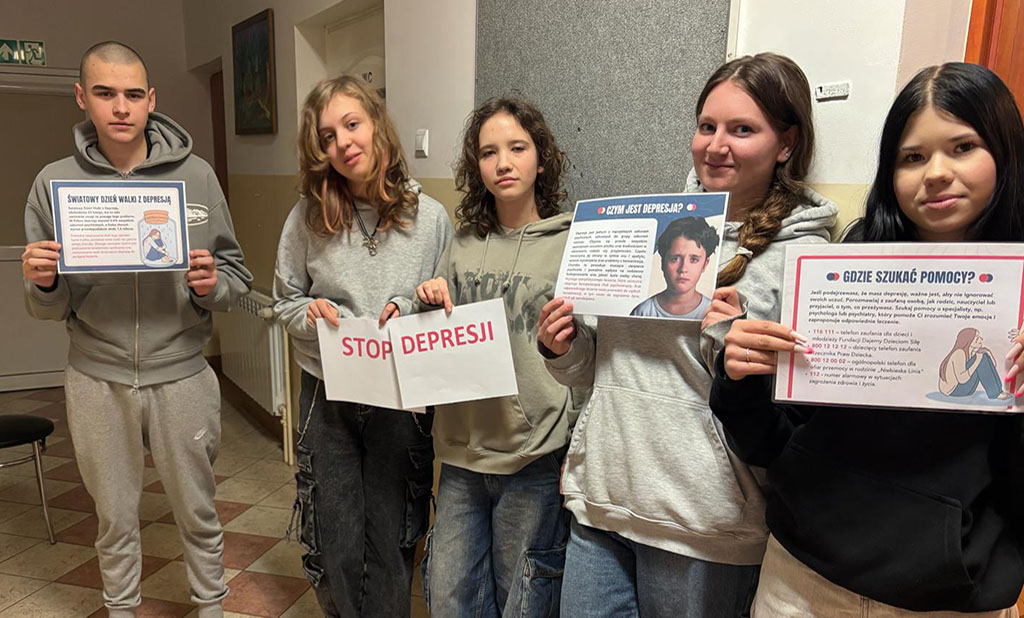 Grupa wychowanków bursy szkolnej prezentuje plakaty informacyjne dotyczące depresji oraz hasło „Stop depresji”. Na kolejnych zdjęciach jedna z uczestniczek przypina materiały edukacyjne na tablicy informacyjnej na korytarzu bursy. Plansze zawierają informacje o objawach depresji, sposobach szukania pomocy oraz profilaktyce.