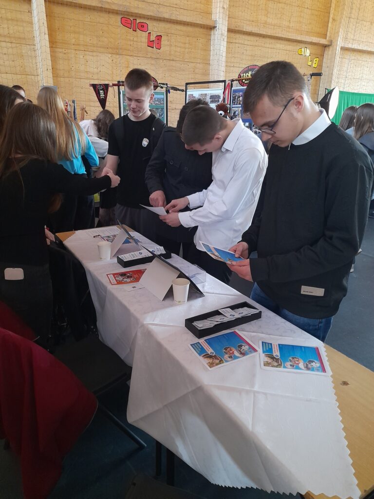 Stoisko Bursy Szkolnej w Miechowie podczas Powiatowych Targów Edukacji – przedstawiciele bursy udzielają informacji odwiedzającym, prezentują materiały promocyjne oraz odpowiadają na pytania dotyczące warunków pobytu i oferty placówki