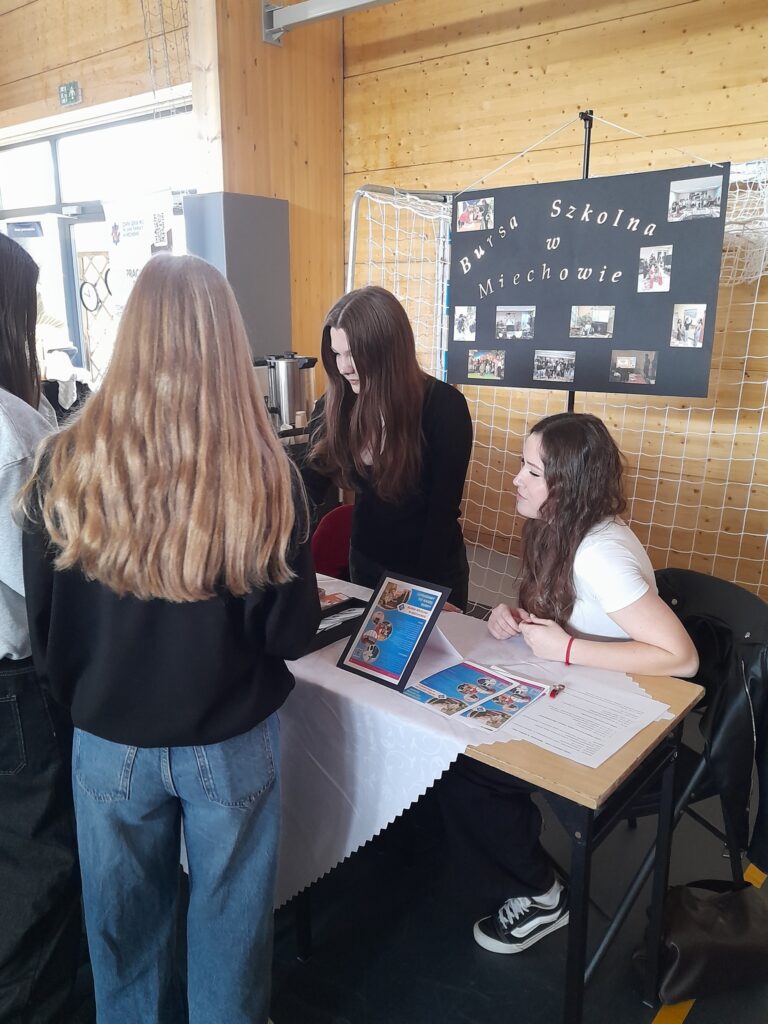Stoisko Bursy Szkolnej w Miechowie podczas Powiatowych Targów Edukacji – przedstawiciele bursy udzielają informacji odwiedzającym, prezentują materiały promocyjne oraz odpowiadają na pytania dotyczące warunków pobytu i oferty placówki