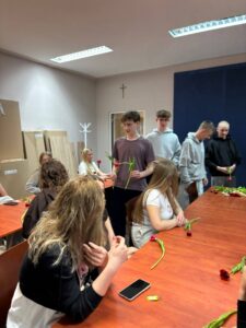 Uczniowie bursy podczas obchodów Dnia Kobiet – chłopcy wręczają dziewczętom tulipany i drobne upominki, wspólne rozmowy przy stołach oraz wieczór filmowy. Na jednym ze zdjęć widoczna jest również gazetka tematyczna poświęcona historii i znaczeniu Dnia Kobiet. Zdjęcia przedstawiają miłą, radosną atmosferę wspólnego świętowania.