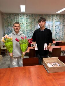 Uczniowie bursy podczas obchodów Dnia Kobiet – chłopcy wręczają dziewczętom tulipany i drobne upominki, wspólne rozmowy przy stołach oraz wieczór filmowy. Na jednym ze zdjęć widoczna jest również gazetka tematyczna poświęcona historii i znaczeniu Dnia Kobiet. Zdjęcia przedstawiają miłą, radosną atmosferę wspólnego świętowania.