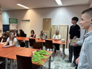 Uczniowie bursy podczas obchodów Dnia Kobiet – chłopcy wręczają dziewczętom tulipany i drobne upominki, wspólne rozmowy przy stołach oraz wieczór filmowy. Na jednym ze zdjęć widoczna jest również gazetka tematyczna poświęcona historii i znaczeniu Dnia Kobiet. Zdjęcia przedstawiają miłą, radosną atmosferę wspólnego świętowania.