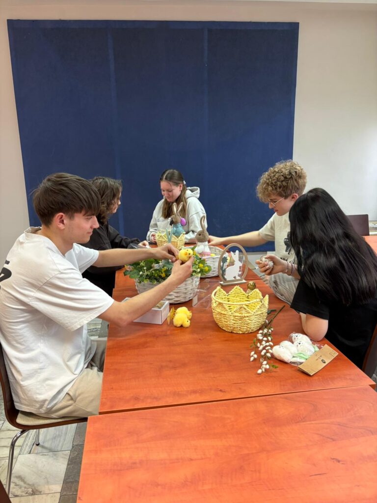 Wychowankowie bursy szkolnej podczas warsztatów wielkanocnych wykonują ręcznie stroiki świąteczne z motywami wiosennymi, takimi jak zajączki, pisanki i kurczaczki. Na zdjęciach widoczne są efekty ich pracy oraz wspólne zaangażowanie w tworzenie dekoracji w sali zajęć i przed budynkiem placówki