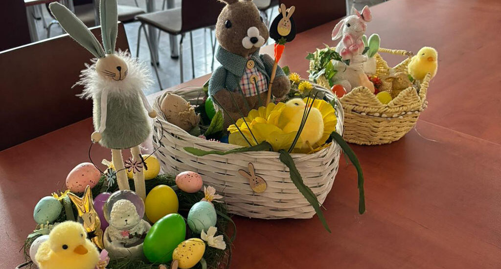 Wychowankowie bursy szkolnej podczas warsztatów wielkanocnych wykonują ręcznie stroiki świąteczne z motywami wiosennymi, takimi jak zajączki, pisanki i kurczaczki. Na zdjęciach widoczne są efekty ich pracy oraz wspólne zaangażowanie w tworzenie dekoracji w sali zajęć i przed budynkiem placówki