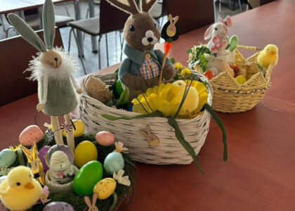 Wychowankowie bursy szkolnej podczas warsztatów wielkanocnych wykonują ręcznie stroiki świąteczne z motywami wiosennymi, takimi jak zajączki, pisanki i kurczaczki. Na zdjęciach widoczne są efekty ich pracy oraz wspólne zaangażowanie w tworzenie dekoracji w sali zajęć i przed budynkiem placówki