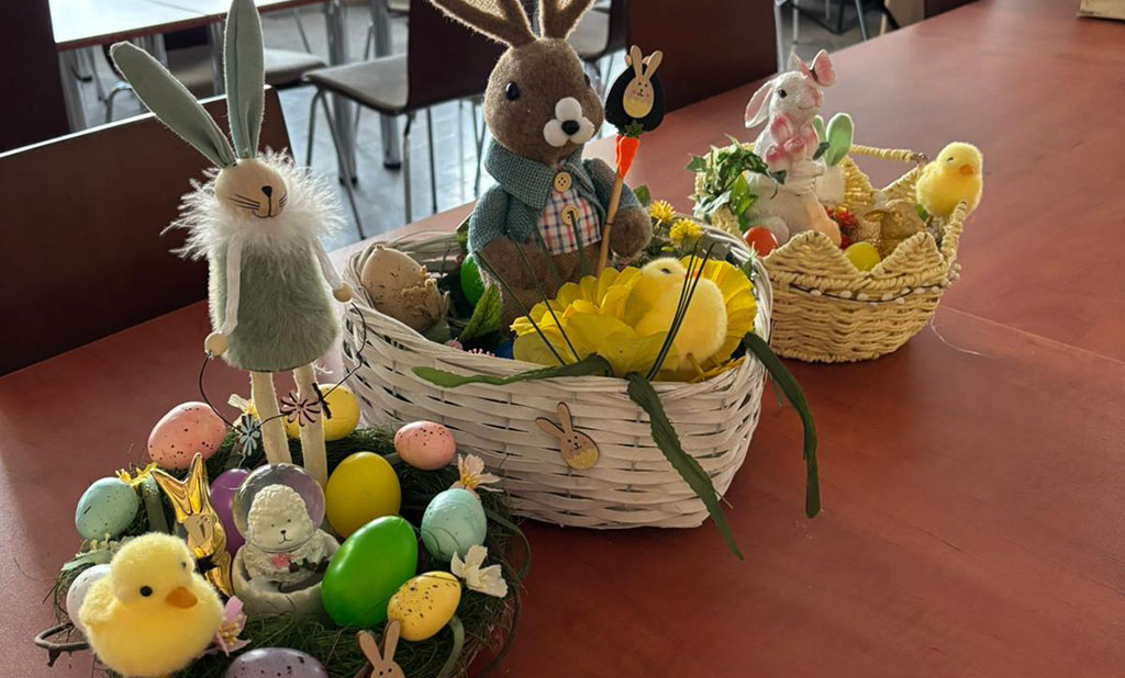 Wychowankowie bursy szkolnej podczas warsztatów wielkanocnych wykonują ręcznie stroiki świąteczne z motywami wiosennymi, takimi jak zajączki, pisanki i kurczaczki. Na zdjęciach widoczne są efekty ich pracy oraz wspólne zaangażowanie w tworzenie dekoracji w sali zajęć i przed budynkiem placówki