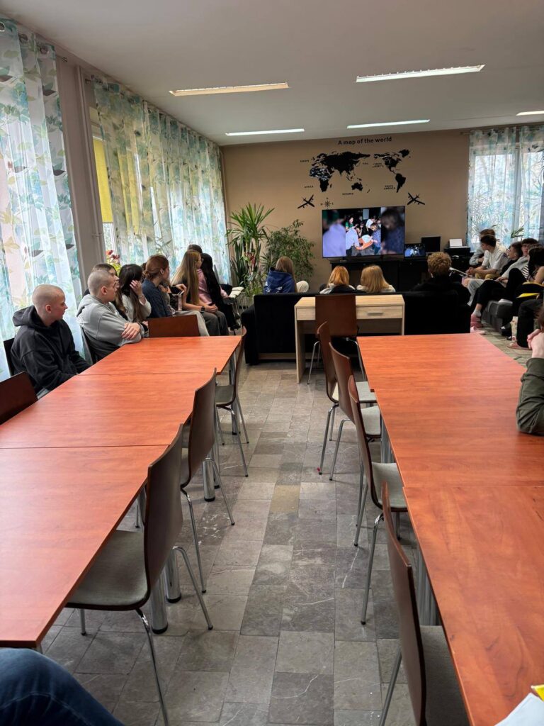 Zdjęcia przedstawiają uroczystość pożegnania maturzystów w Bursie Szkolnej. W sali z ustawionymi stołami i krzesłami grupa młodzieży oraz wychowawcy uczestniczą w oficjalnym spotkaniu. Na jednej z fotografii uczennica trzyma upominek, na innych widoczne jest wręczanie prezentów oraz odczytywanie przemówień i podziękowań. Na stołach znajdują się torby z upominkami. W tle widoczna jest tablica oraz elementy wyposażenia sali. Atmosfera wydarzenia ma charakter uroczysty i podniosły