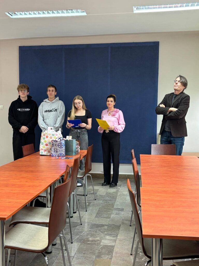 Zdjęcia przedstawiają uroczystość pożegnania maturzystów w Bursie Szkolnej. W sali z ustawionymi stołami i krzesłami grupa młodzieży oraz wychowawcy uczestniczą w oficjalnym spotkaniu. Na jednej z fotografii uczennica trzyma upominek, na innych widoczne jest wręczanie prezentów oraz odczytywanie przemówień i podziękowań. Na stołach znajdują się torby z upominkami. W tle widoczna jest tablica oraz elementy wyposażenia sali. Atmosfera wydarzenia ma charakter uroczysty i podniosły