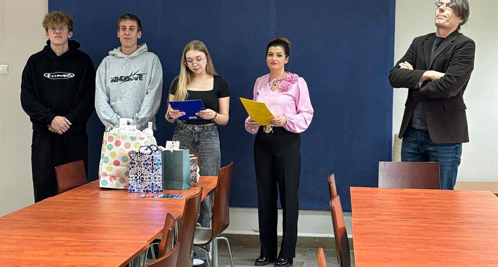 Zdjęcia przedstawiają uroczystość pożegnania maturzystów w Bursie Szkolnej. W sali z ustawionymi stołami i krzesłami grupa młodzieży oraz wychowawcy uczestniczą w oficjalnym spotkaniu. Na jednej z fotografii uczennica trzyma upominek, na innych widoczne jest wręczanie prezentów oraz odczytywanie przemówień i podziękowań. Na stołach znajdują się torby z upominkami. W tle widoczna jest tablica oraz elementy wyposażenia sali. Atmosfera wydarzenia ma charakter uroczysty i podniosły