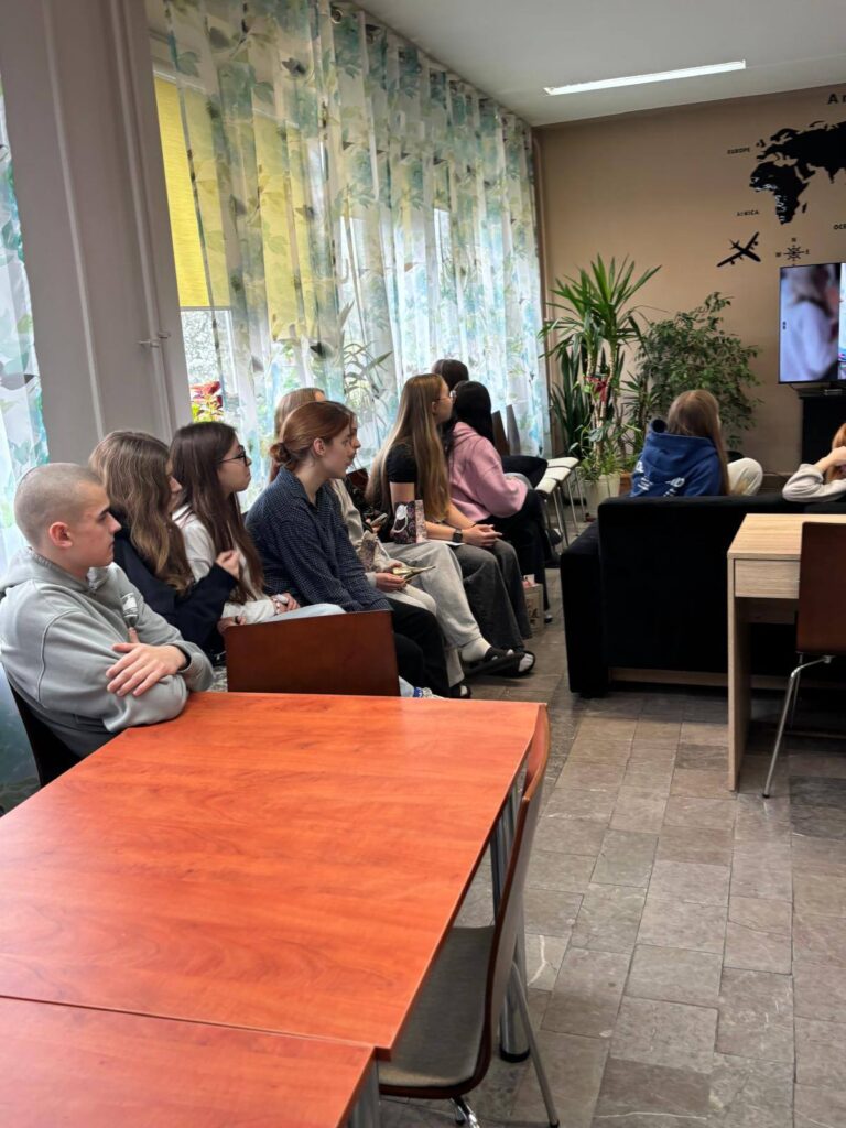 Zdjęcia przedstawiają uroczystość pożegnania maturzystów w Bursie Szkolnej. W sali z ustawionymi stołami i krzesłami grupa młodzieży oraz wychowawcy uczestniczą w oficjalnym spotkaniu. Na jednej z fotografii uczennica trzyma upominek, na innych widoczne jest wręczanie prezentów oraz odczytywanie przemówień i podziękowań. Na stołach znajdują się torby z upominkami. W tle widoczna jest tablica oraz elementy wyposażenia sali. Atmosfera wydarzenia ma charakter uroczysty i podniosły