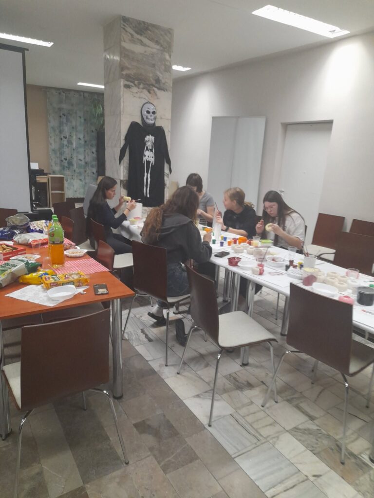 Wychowankowie Bursy Szkolnej w Miechowie podczas warsztatów artystyczno-integracyjnych z okazji Halloween. Zdjęcia przedstawiają zbieranie dyń w gospodarstwie rolnym, tworzenie halloweenowych lampionów, malowanie ozdób gipsowych oraz wspólną pracę i integrację młodzieży podczas zajęć.