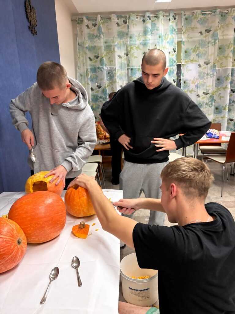 Wychowankowie Bursy Szkolnej w Miechowie podczas warsztatów artystyczno-integracyjnych z okazji Halloween. Zdjęcia przedstawiają zbieranie dyń w gospodarstwie rolnym, tworzenie halloweenowych lampionów, malowanie ozdób gipsowych oraz wspólną pracę i integrację młodzieży podczas zajęć.